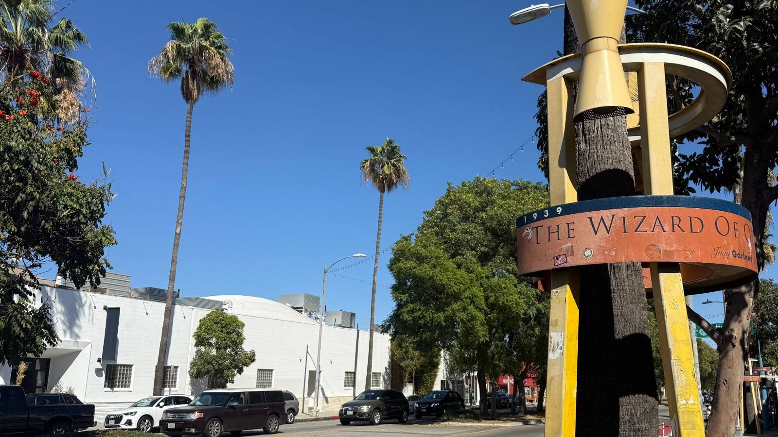 Washington Boulevard in the Culver City Arts District on a sunny day, with tall palm trees, parked cars, and a Wizard of Oz sculpture on a tall pole at the right