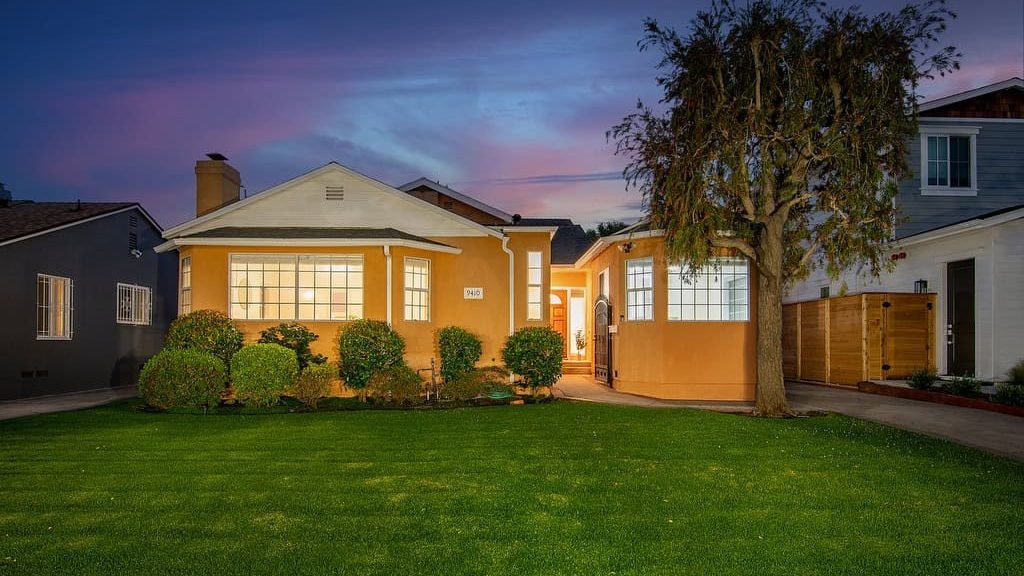 Orange house with a lit front window and a green lawn at dusk